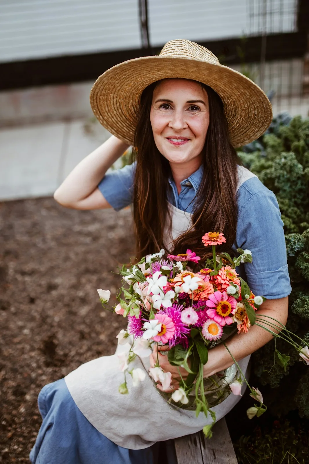 Frau mit Strohhut und Blumenstrauß im Garten, lächelnd