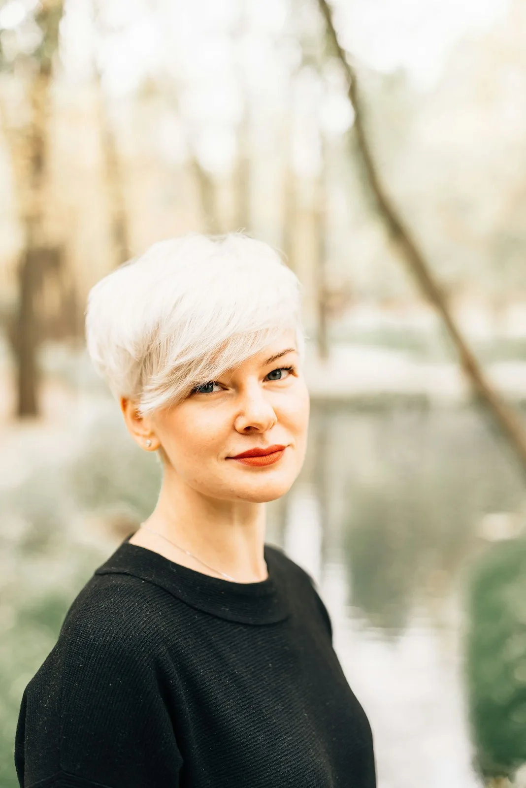 Frau mit kurzem weißblondem Haar vor herbstlichem Wasser