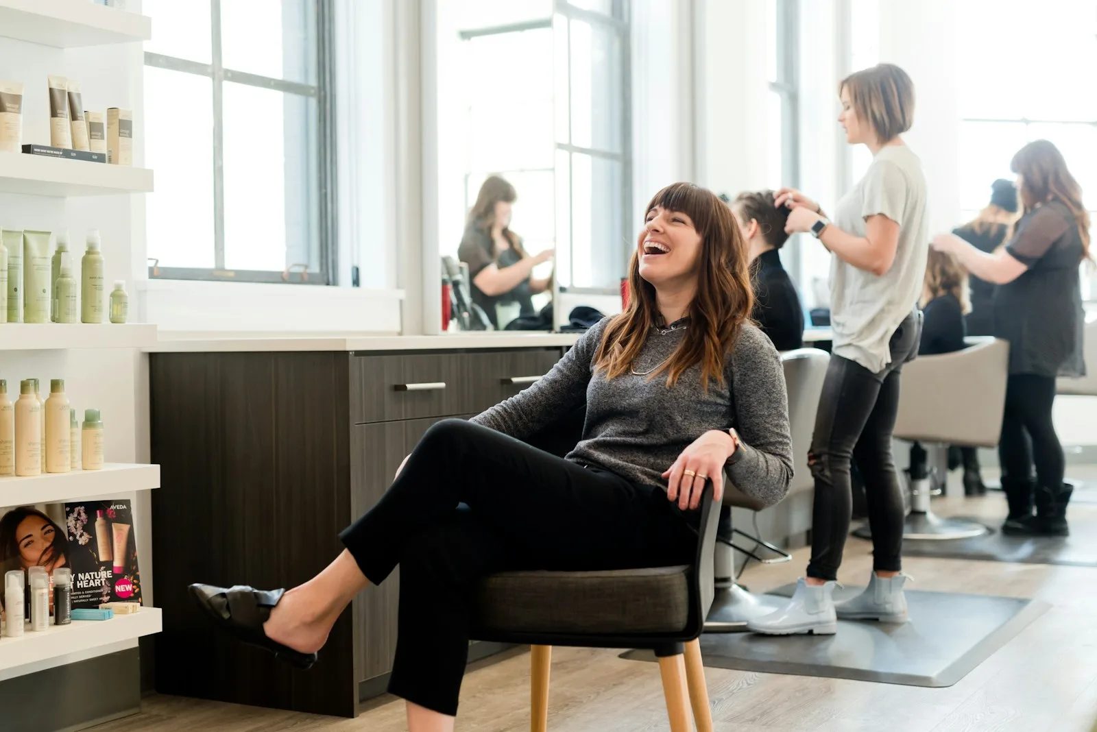 Frau sitzt lachend auf einem Stuhl im hellen Salon am Fenster