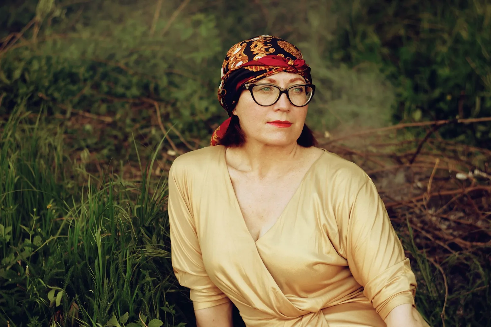Frau mit Kopftuch und Brille sitzt im goldenen Abendlicht im Gras