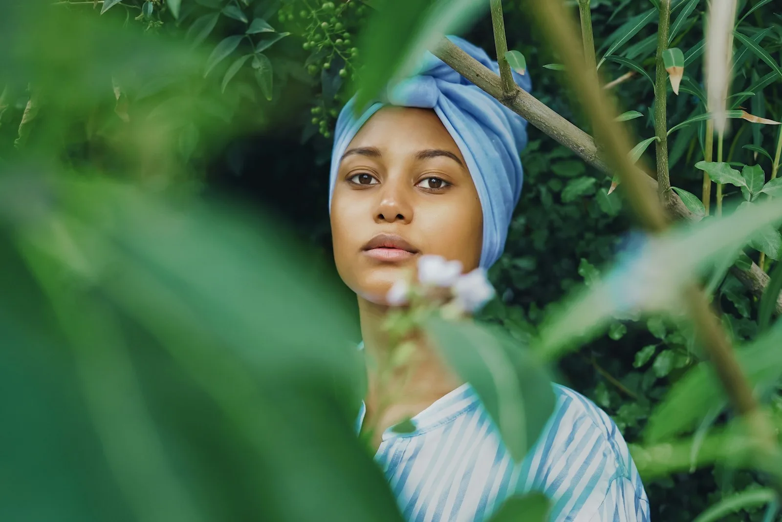 Frau mit hellblauem Turban zwischen grünen Blättern