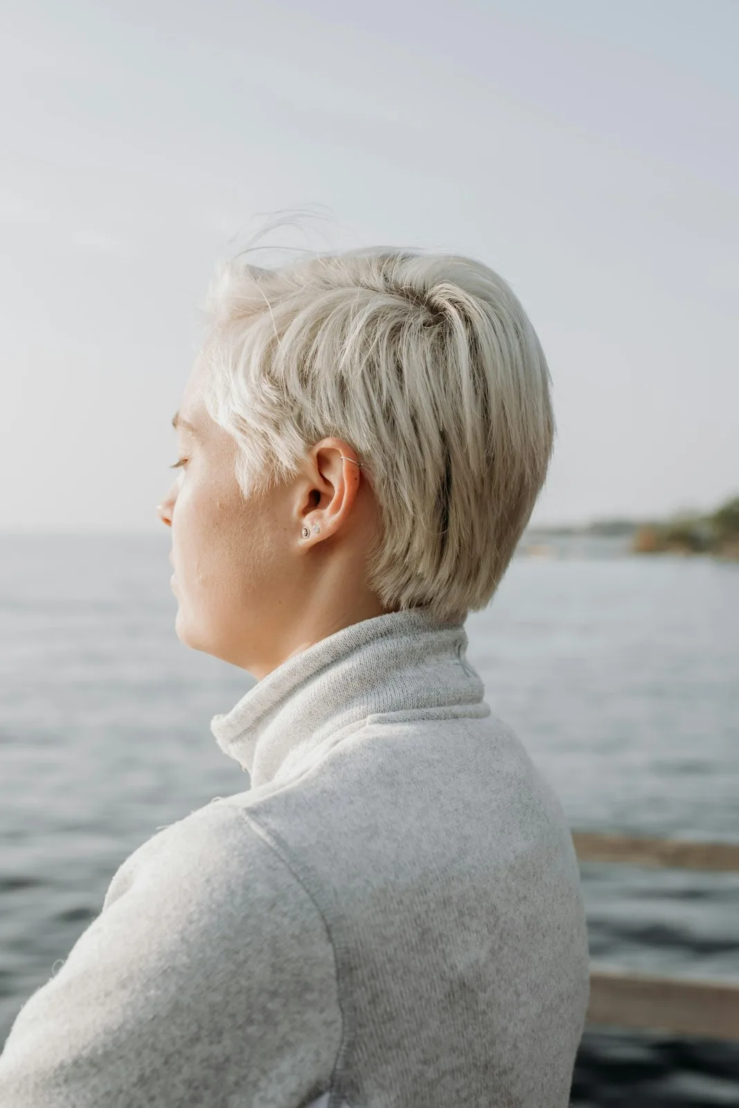 Frau mit weißem kurzem Haar blickt von hinten aufs Meer